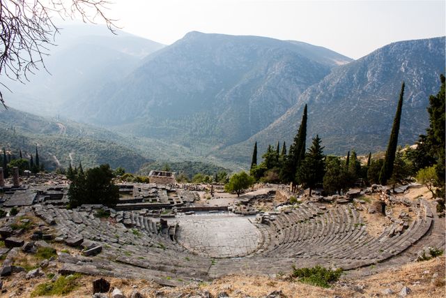 Depicts ancient Greek amphitheater against backdrop of towering mountains and lush landscape. Perfect for historical studies, travel brochures, cultural heritage documentation, educational materials, and visual content promoting tourism to Greece.