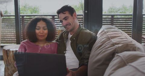 Couple relaxing on sectional sofa sharing laptop, cozy home workspace with natural wood accents