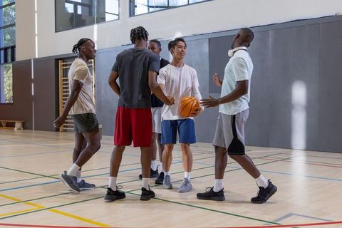 Multiracial male friends huddling on indoor basketball court, sharing moment after game