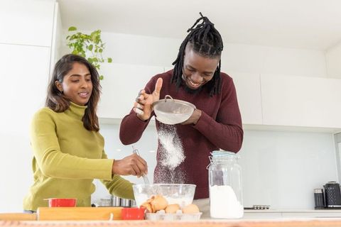 Couple baking together in bright modern kitchen sifting flour and whisking batter