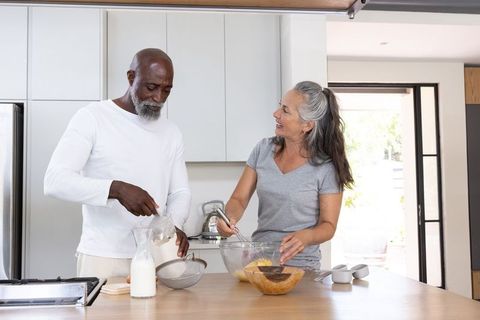 Sunlit diverse senior couple cooking breakfast together on modern kitchen island