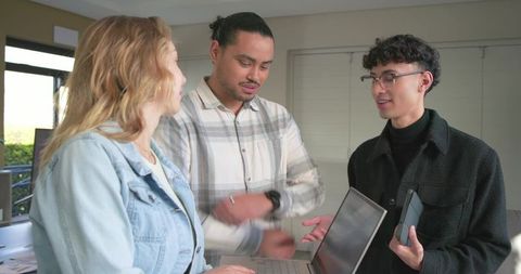 Diverse team collaborating around open laptop in bright home office for remote work