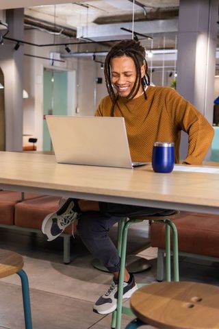 Smiling African American Man Working on Laptop in Modern Coworking Lounge for Remote Work