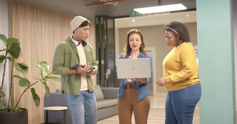 Diverse coworkers discussing project around open laptop in modern office lounge
