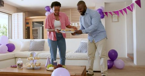 African American couple preparing birthday party with purple balloons, cupcakes and desserts