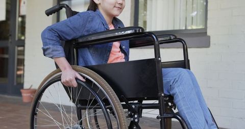 Youth pushing manual wheelchair on porch, gripping wheel rim and practicing mobility independence