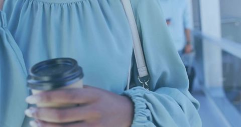 Woman holding coffee cup while walking through airport corridor wearing teal blouse