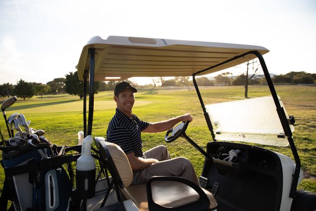 Caucasian male golfer wearing a cap and golf clothes, driving a golf cart on a sunny day. Ideal for use in advertisements, sports magazines, lifestyle blogs, and promotional materials related to golf, outdoor activities, and healthy living.