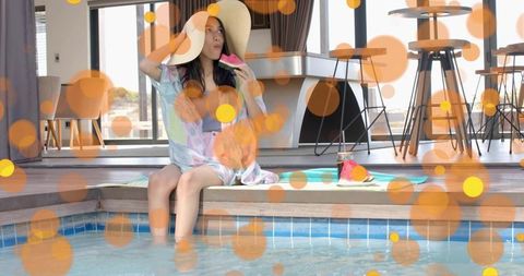 Woman sitting poolside in straw hat dipping feet eating watermelon relaxing on deck