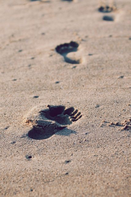 Footprints on sandy beach captured at ideally during sunset, evoking feelings of solitude and adventure. Suitable for use in travel brochures, vacation promos, and inspirational wall art.
