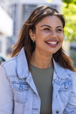 Sunlit african american woman smiling on urban sidewalk wearing denim jacket