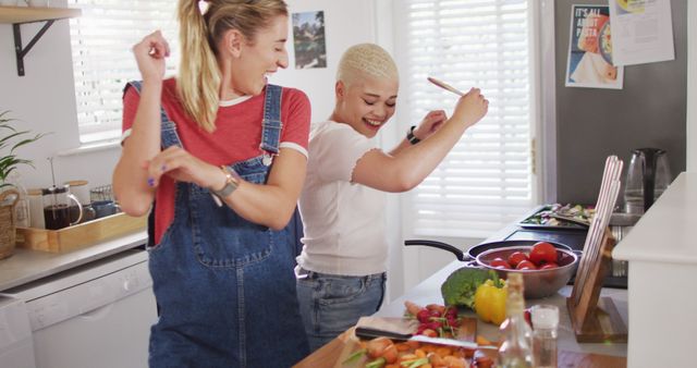 Happy diverse female couple cooking vegetables and dancing in kitchen - Download Free Stock Photos Pikwizard.com