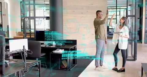 High-fiving coworkers celebrating project win in modern open-plan tech office with glass walls