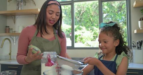 Mother and daughter baking together, sifting flour and mixing batter in sunlit kitchen