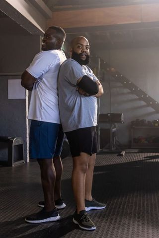 African american fitness duo standing back-to-back in gym showing strength and teamwork