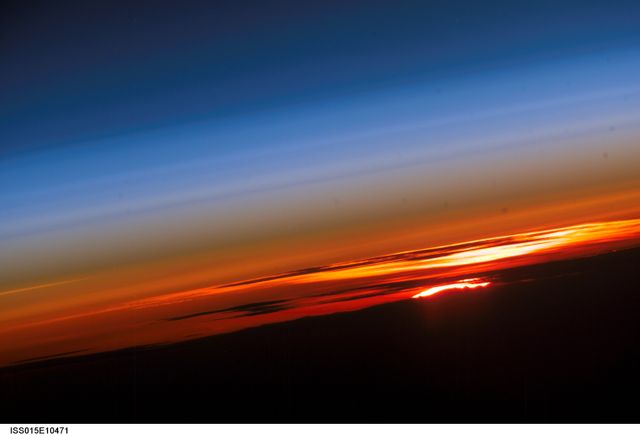 Stunning view of sunset over Earth's horizon captured by Expedition 15 crew on the International Space Station, showing vibrant atmospheric layers. Perfect for articles or educational materials on space exploration, atmospheric science, and astrophotography. Also suitable for scenic background images or inspiring desktop wallpapers.