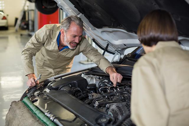 Mechanics examining car engine in repair shop, showcasing teamwork and expertise in automotive maintenance. Ideal for use in articles, advertisements, and websites related to car repair services, automotive workshops, and professional mechanics.