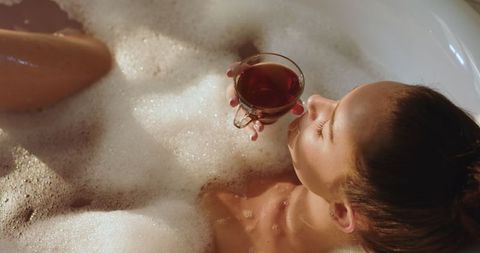 Woman Relaxing in Bubble Bath Holding Glass Teacup by Refined Interiors