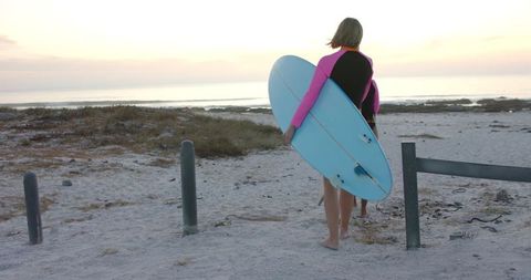 Surfer Walking to Ocean at Sunset with Surfboard