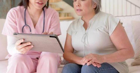 Home Care Nurse Consulting Older Woman Using Tablet During Telehealth Visit in Living Room