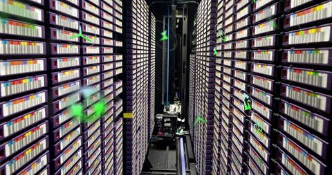 Robotic gantry gliding through tape library aisles with stacked purple cartridge racks