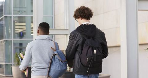 College students walking on campus carrying backpacks and colorful notebooks in city plaza