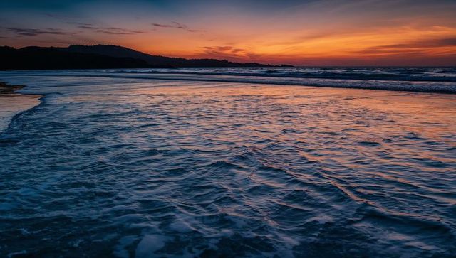 Sunset reflecting on rippled shoreline with gentle waves lapping headland silhouette