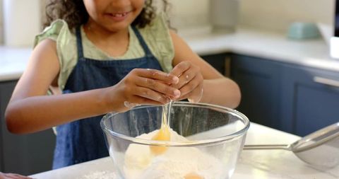 African american girl cracking egg while baking with flour in glass mixing bowl