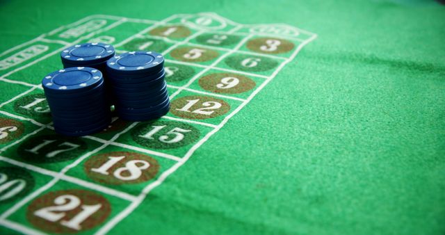Blue casino chips stacked on green felt surface of blackjack table, numbers visible. Suitable for articles about casinos, gambling strategies, or luck. Ideal for use in promotional materials for gaming or casino events, illustrating themes of betting and winning.
