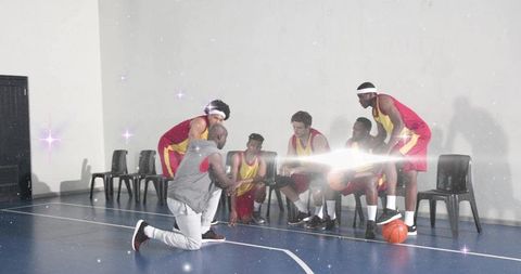 Kneeling coach coaching college basketball team in red yellow jerseys on indoor court