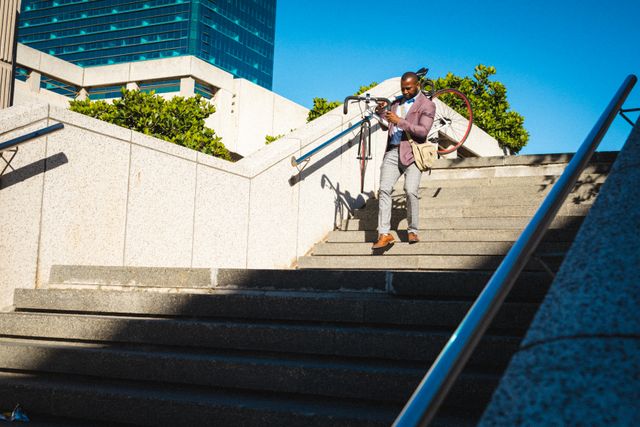 Businessman in a suit carrying his bicycle down concrete stairs in a corporate park. Ideal for use in articles about urban commuting, professional lifestyles, sustainable transportation, and modern business environments.