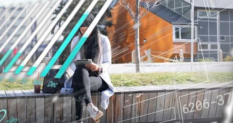 Young woman studying on urban bench using tablet with iced coffee and digital data overlay