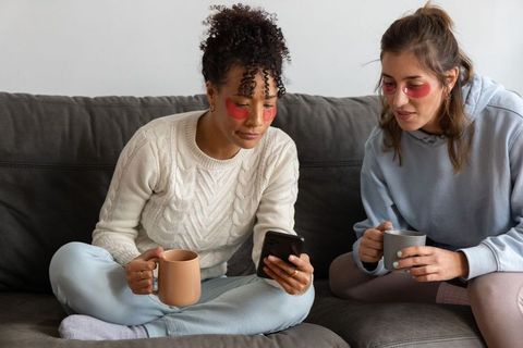 Diverse women sharing cozy self-care moment wearing under-eye patches and sipping coffee
