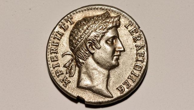 Silver laurel-bust coin close-up on neutral surface, numismatic relief, patina and chip