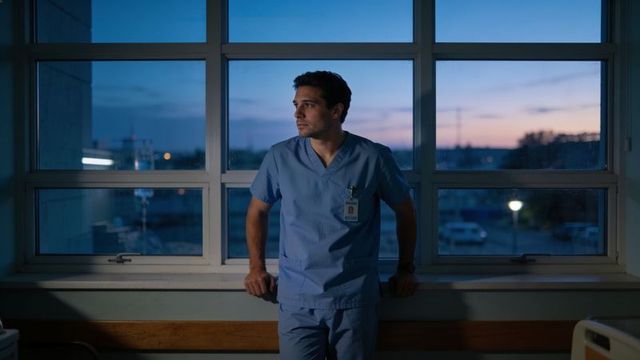 Leaning clinician gazing out hospital window at dusk contemplating night shift