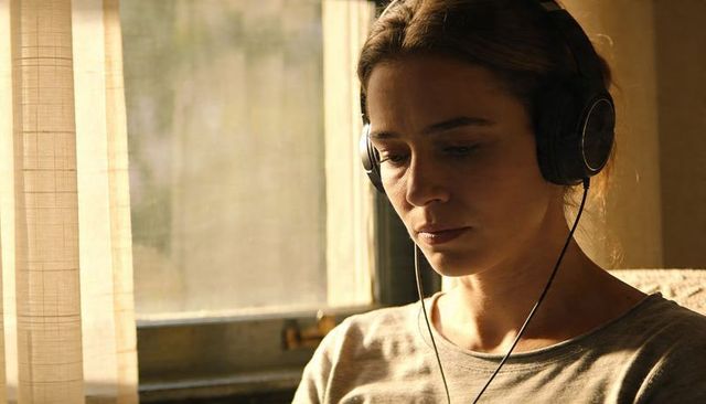 Sunlit woman listening on headphones by window, reflective calm and warm mood