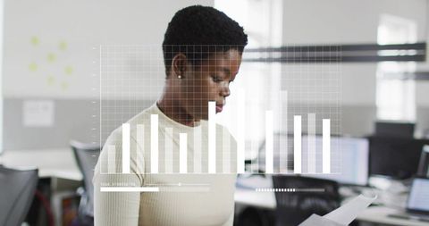 African woman analyzing bar chart overlay while holding document in modern open office