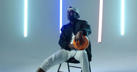 Urban Athlete Clad in Sportswear Holding Basketball Amid Neon Lights