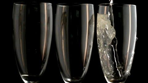 Three Champagne Flutes with One Being Filled on Black Background