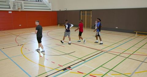 Five male basketball players walking across indoor gym court practicing teamwork drills