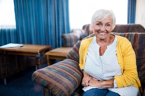 Senior woman relaxing at home in yellow cardigan by sunny window
