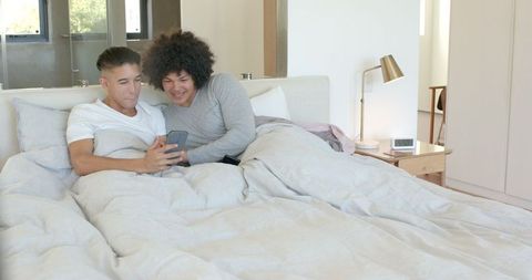 Diverse Male Partners Relaxing in Bed with Smartphone