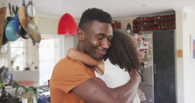 Smiling african american father hugging daughter in kitchen. Fatherhood, childhood, care, love, togetherness and domestic life.