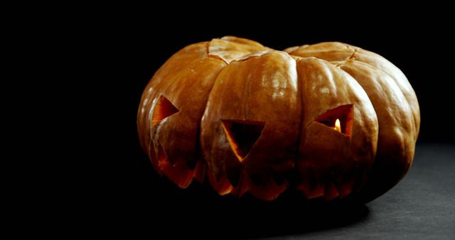 A carved pumpkin with a menacing face glows ominously against a dark background, with copy space. Its flickering light creates a spooky atmosphere, often associated with Halloween celebrations.