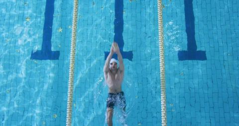 Aerial view of swimmer streamlining through sunlit lap pool with lane ropes and reflections
