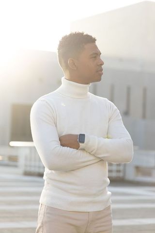 African American man standing on sunlit rooftop crossing arms in turtleneck and smartwatch