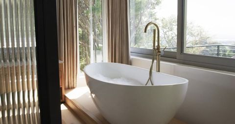 Freestanding oval bathtub on raised timber plinth with brass floor faucet and foam