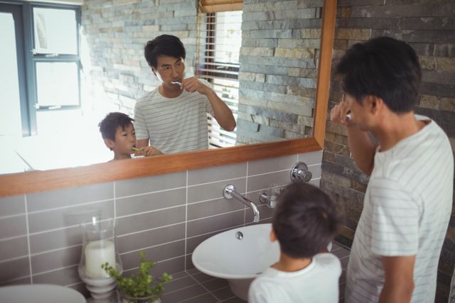 Father and son brushing teeth together in bathroom at home