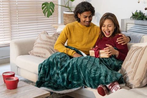 Cozy diverse couple sharing gift on sofa under plush green blanket
