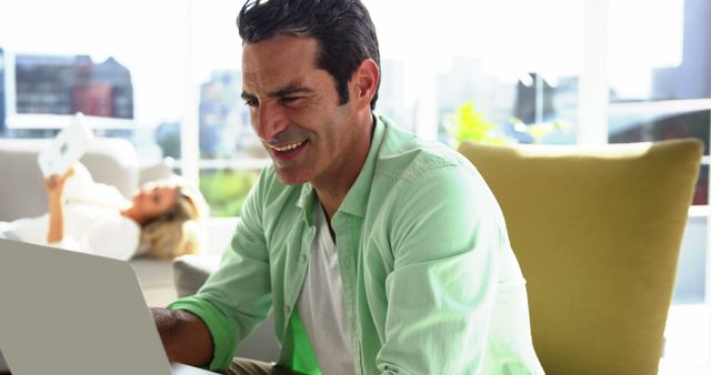 Man Working on Laptop at Home with Woman Relaxing in Background - Download Free Stock Images Pikwizard.com